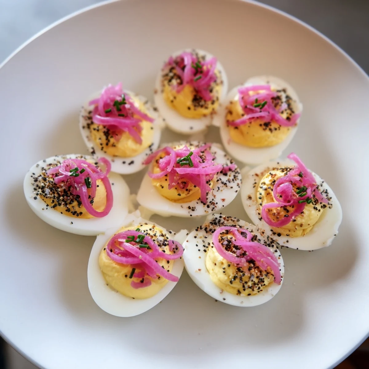 Bright and creamy Everything-Spiced Deviled Eggs, garnished with chives and pickled shallots for an appetizing photo.