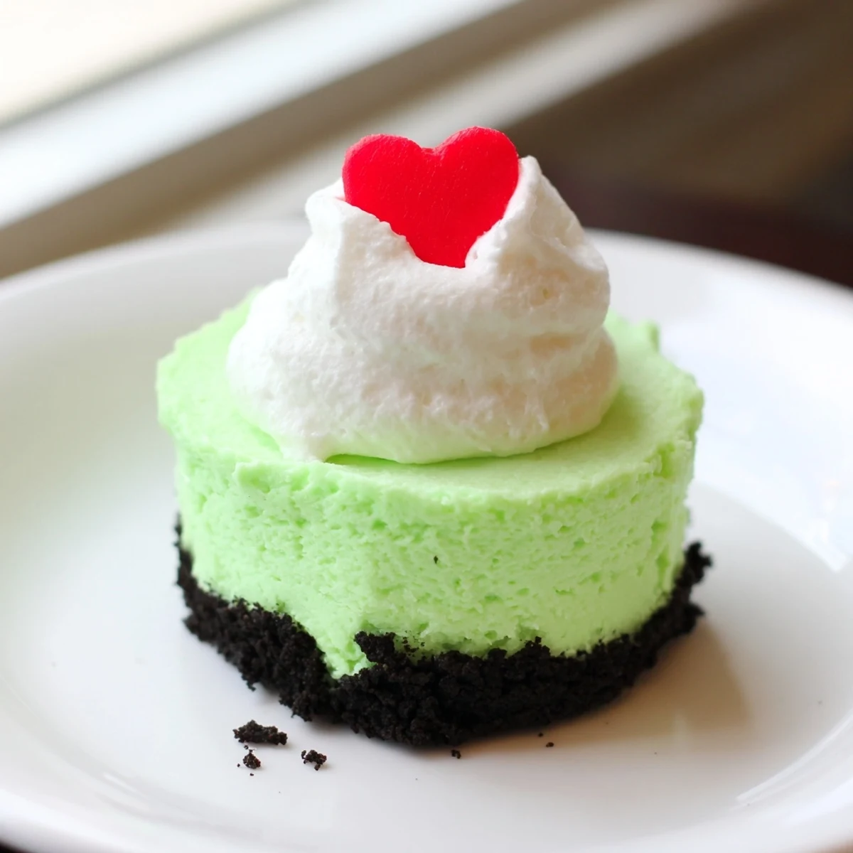 Bright green Grinch Mini Cheesecakes topped with whipped cream and red heart sprinkles, a festive dessert.