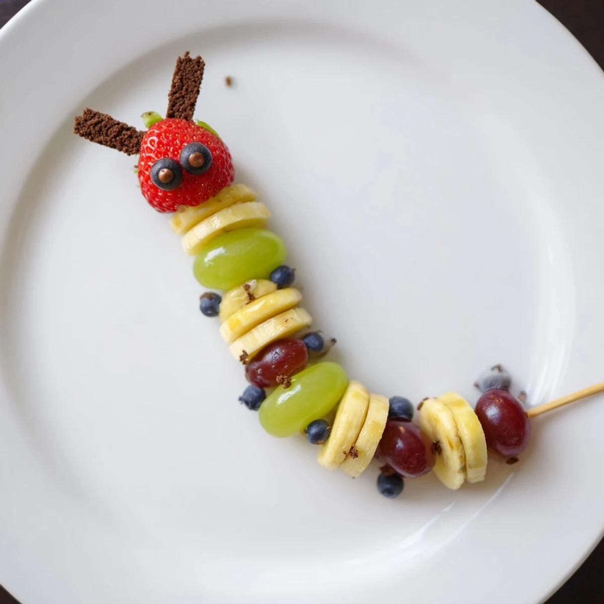 Whimsical Caterpillar Fruit Skewers in process, showcasing fresh fruit along a whimsical trail.