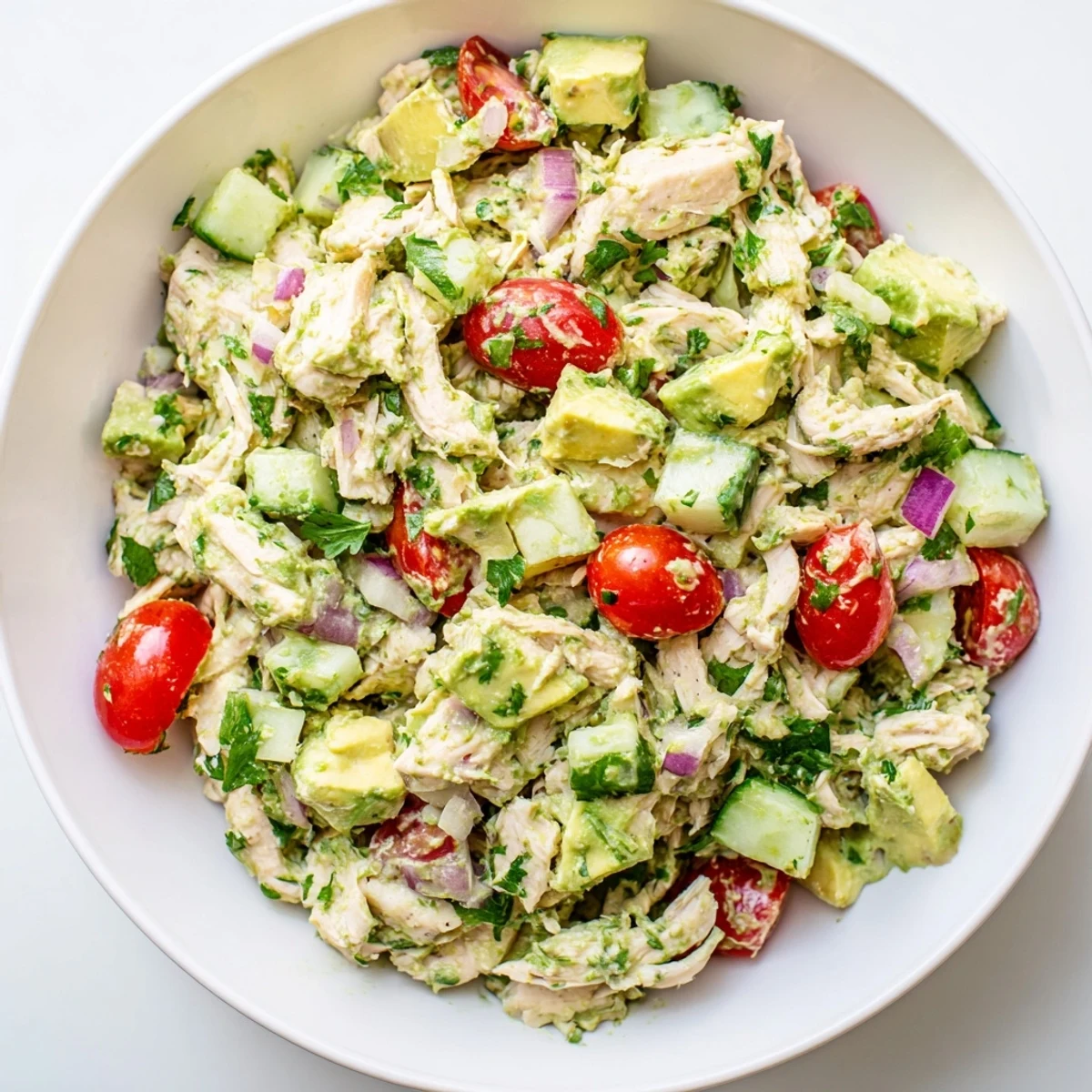 A bowl of colorful avocado chicken salad featuring diced avocado, juicy tomatoes, and a zesty lime dressing.