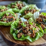 Ready-to-eat Turkey Potsticker Stir-Fry Lettuce Wraps garnished with sesame seeds on a rustic wooden table.
