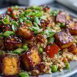 A close-up view of Crispy Sesame Tofu Fried Rice, highlighting the crunchy texture of the tofu and the glossy sesame-ginger sauce coating the grains.