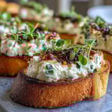 Fresh chives and thyme garnish these easy Hot Honey Goat Cheese Crostini, arranged on a rustic wooden serving board.
