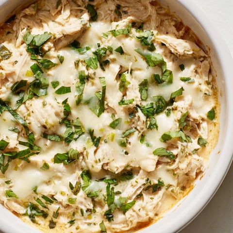 Golden-baked Cilantro and Lime Chicken dip in a white dish, garnished with fresh cilantro and lime wedges, served with tortilla scoops for dipping.