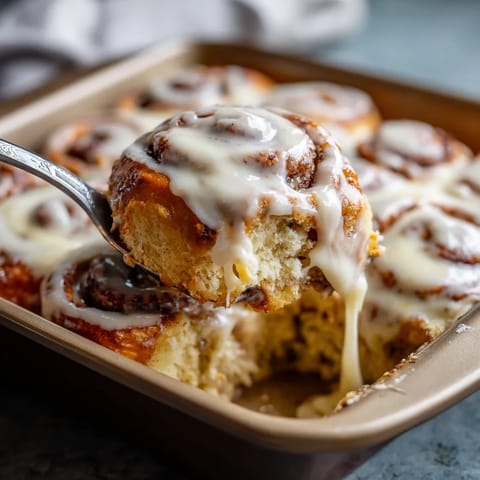 A fork is in a pan of iced cinnamon roll cake.