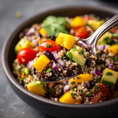 A spoon is in a bowl of quinoa, mango and black bean salad.