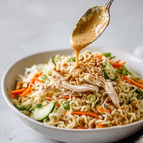 A bowl of noodles with chicken and peanut sauce.