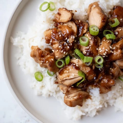 A hearty bowl of slow cooker teriyaki chicken with rice, garnished with green onions and sesame seeds.