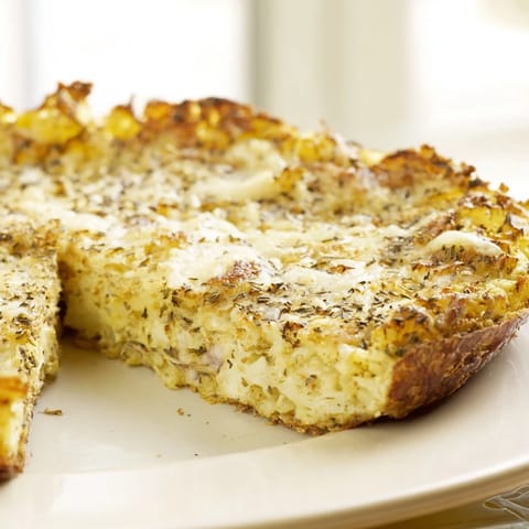 A freshly baked cauliflower pizza crust with bubbly cheese and a variety of colorful vegetable toppings.