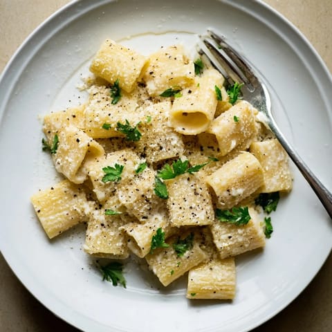 A close-up of creamy milk pasta; the rich, white sauce clings to penne with Parmesan.