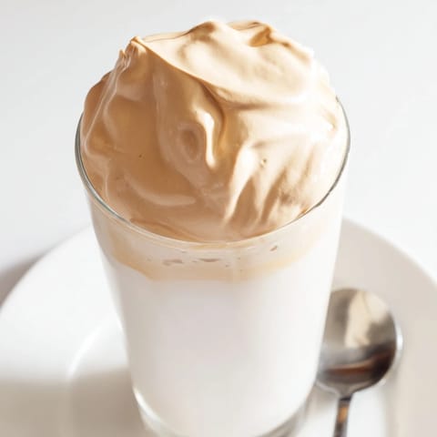 Creamy, cloud-like whipped Dalgona coffee rests on top of cold milk, ready to be enjoyed.
