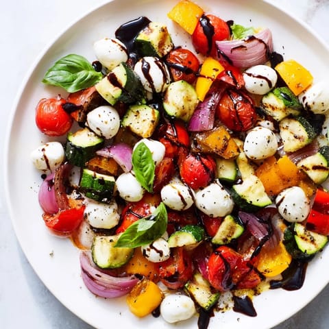 A colorful Roasted Veggie Caprese Salad, showcasing roasted veggies, mozzarella balls, and fresh basil leaves.