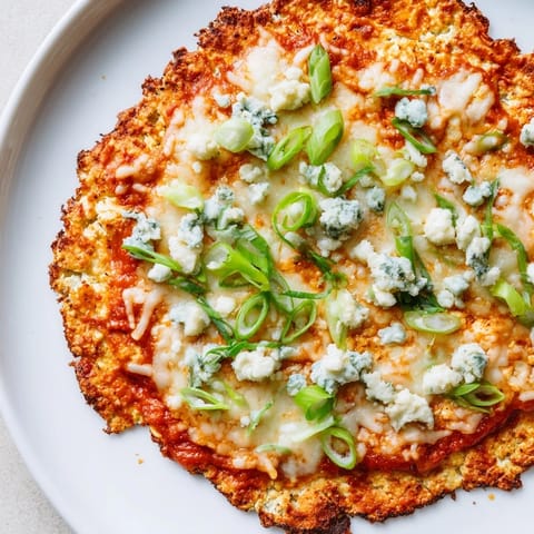 A close-up of a bubbling Buffalo Cauliflower Pizza, with vibrant green onions and celery visible.