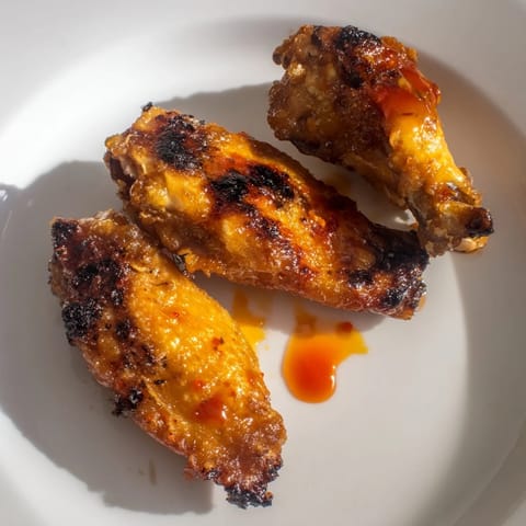 Perfectly fried chicken wings tossed in spicy Buffalo sauce, garnished with sliced scallions on a rustic wooden serving platter.