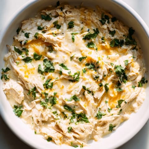 A close-up of Cilantro and Lime Chicken dip showing creamy melted cheese and tender shredded chicken, ready to be scooped up with corn chips.