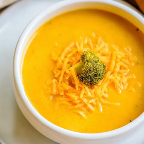 Golden roasted butternut squash and broccoli florets blend into a rich, velvety cheddar soup, garnished with a fresh herb sprig.