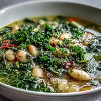 Hearty bowl of kale and white bean soup with lemon and garlic, garnished with fresh parsley and served with crusty bread.  